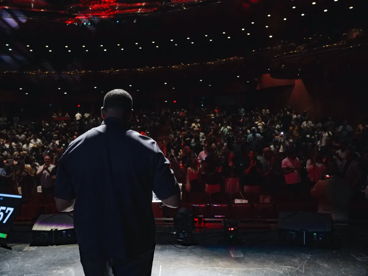 A speaker on stage facing a packed theater at a Team NuVision event