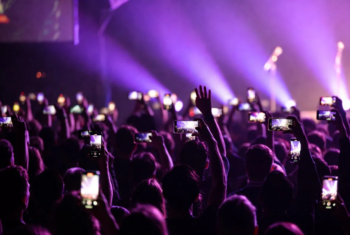 A crowd holding up phones under purple stage lights