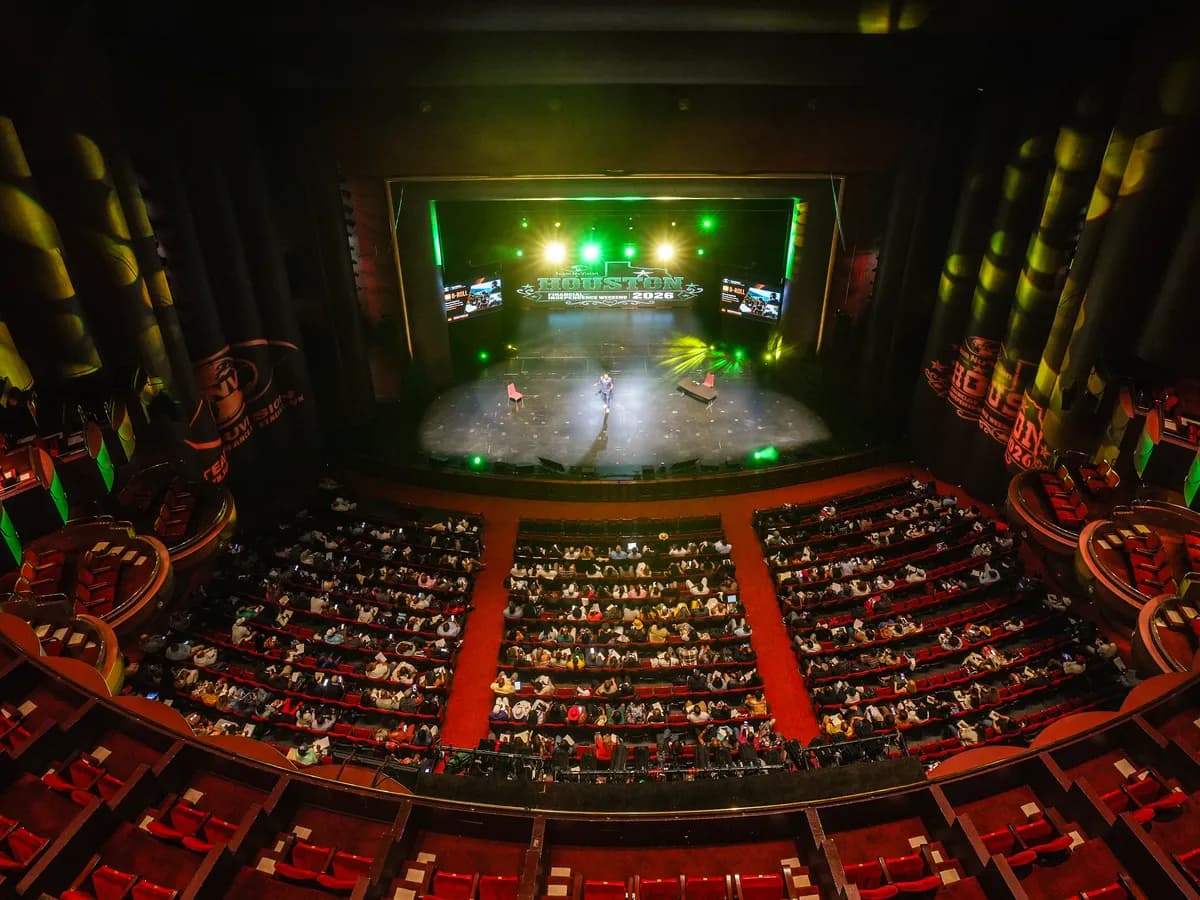 A full theater seen from the balcony, with the stage lit in green