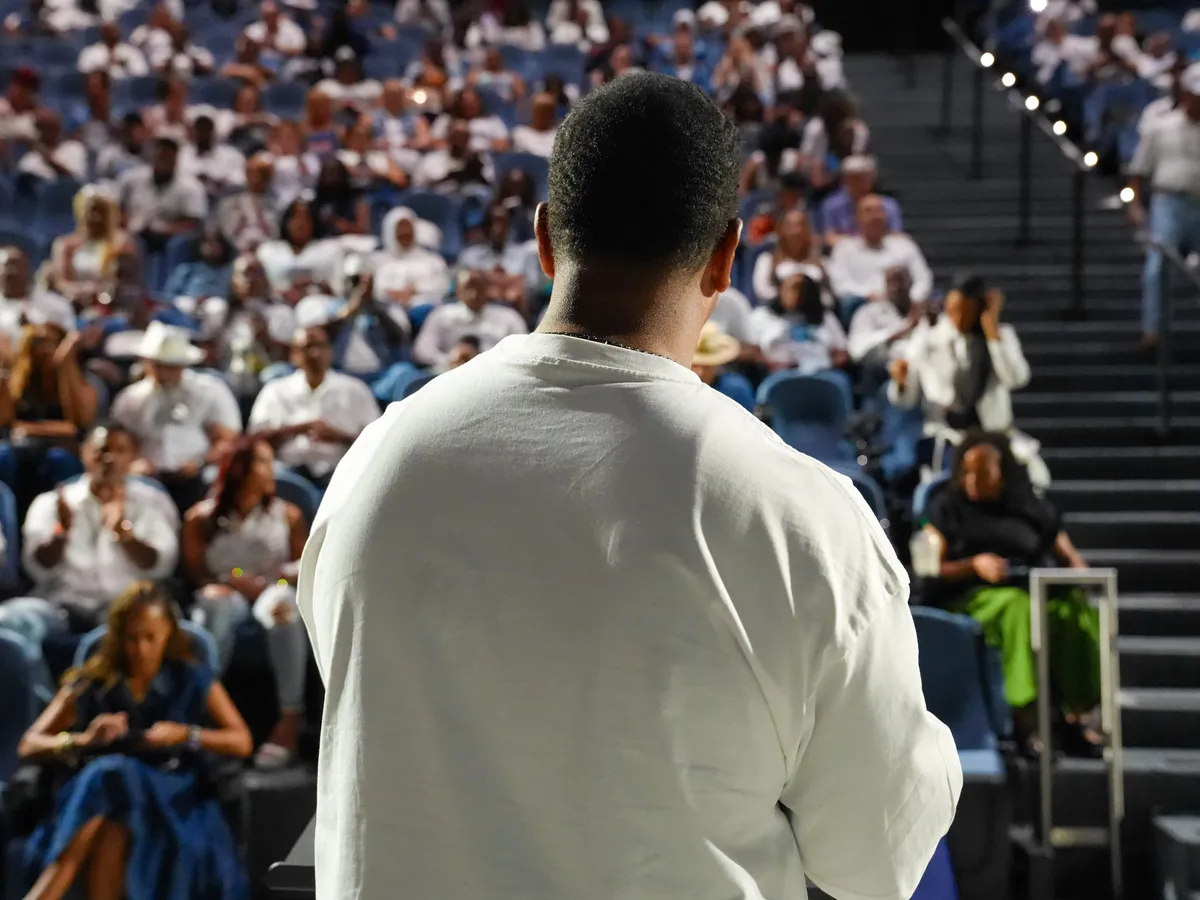 A speaker in white facing a large audience dressed in white